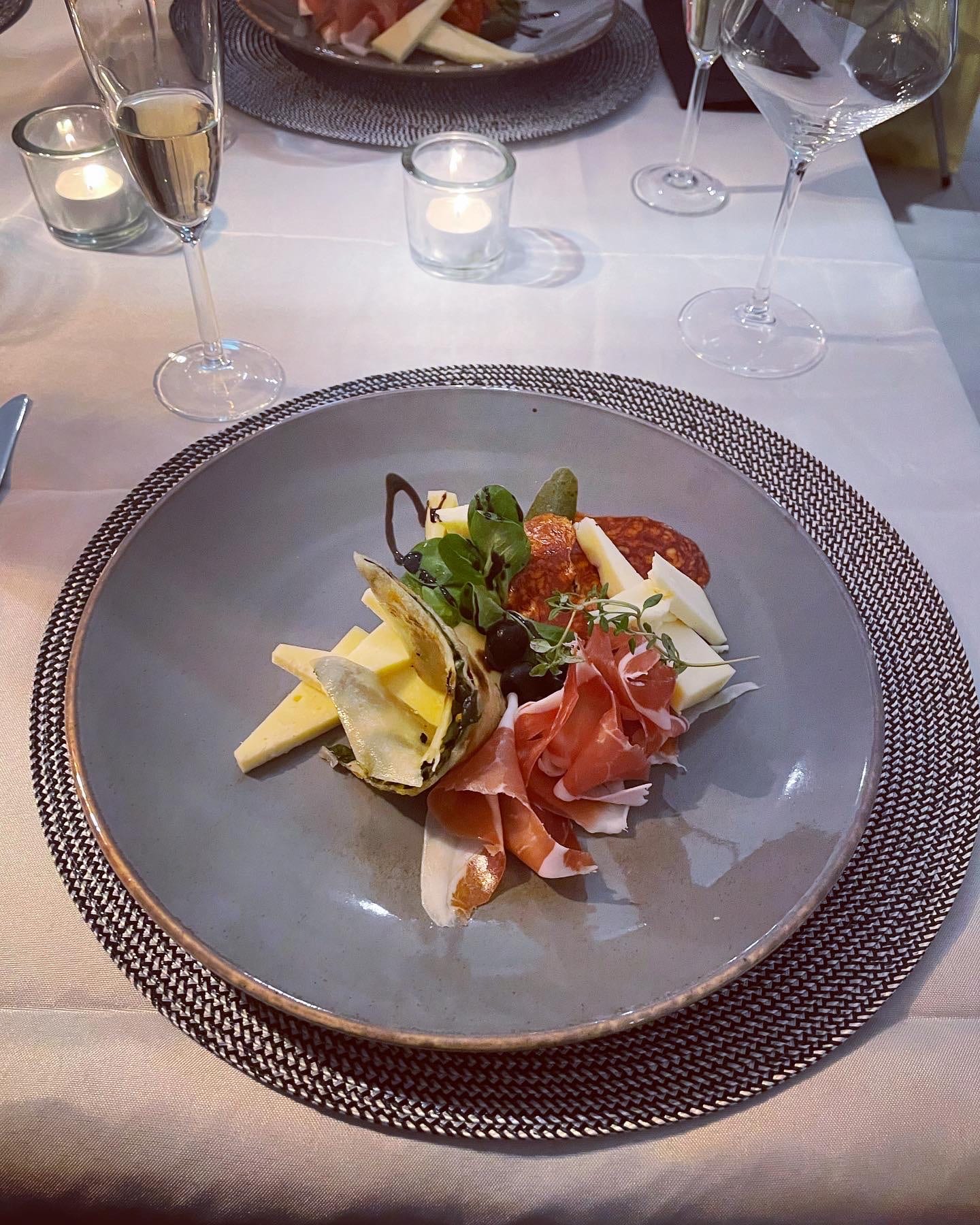 A plated starter of cheese, prosciutto, sausage and olives on the candlelit dinner table