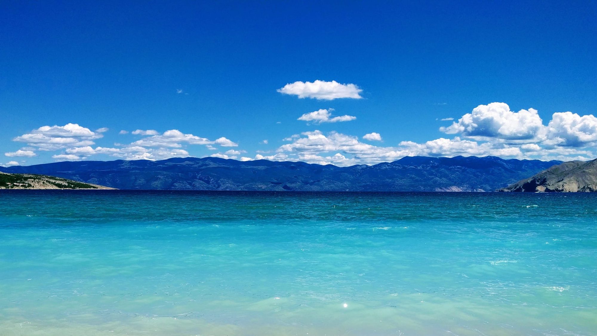 A pebble beach on the Adriatic, with clear shallow water and mountains across the channel